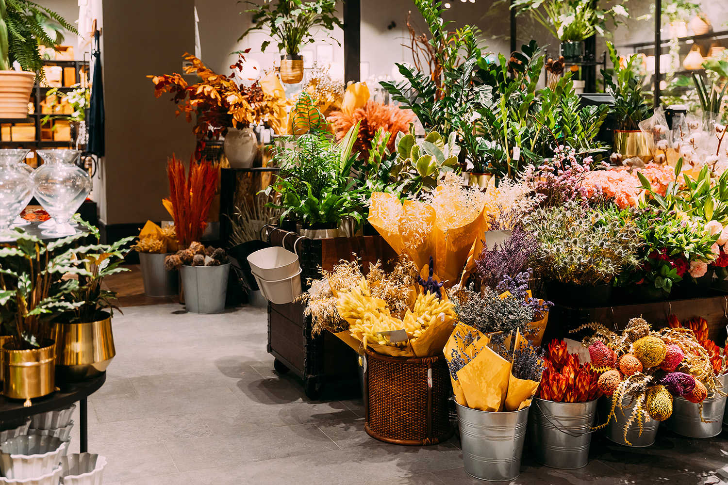 Interior of a flower shop in Manila featuring vibrant floral arrangements, potted plants, and wrapped dried bouquets in metallic buckets